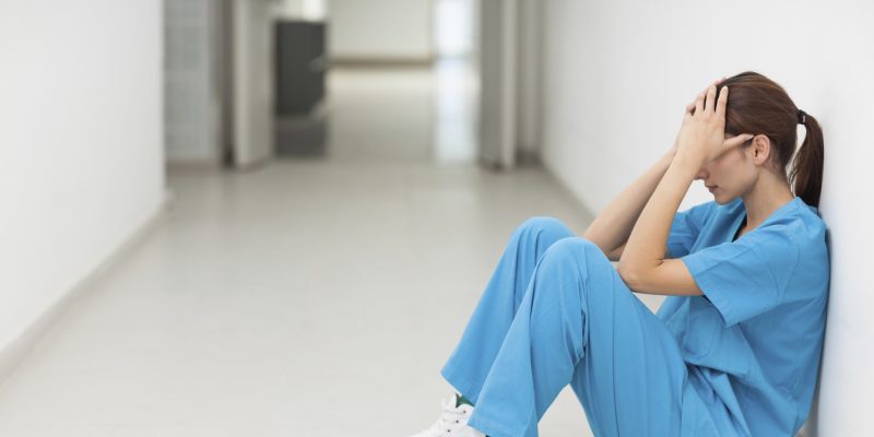 Nurse sitting in a corridor while holding her head