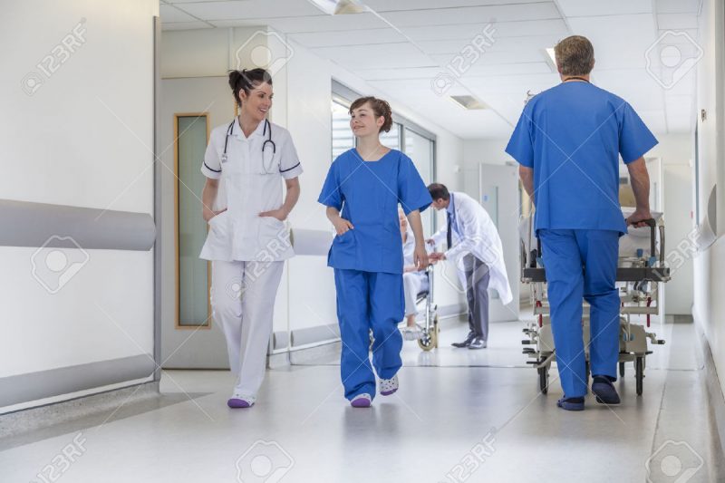 26578311-Male-nurse-pushing-stretcher-gurney-bed-in-hospital-corridor-with-male-female-doctors-nurses-senior--Stock-Photo